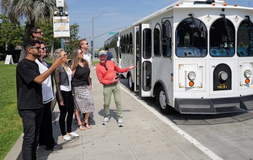 A professional tour guide welcoming a private group of guests onto a vintage-style white Parlor Car Trolley for a personalized tour of Hollywood.